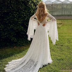 a woman in a white wedding dress standing on grass with her back to the camera