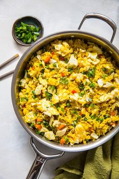 a pan filled with rice and vegetables on top of a white table next to green napkins