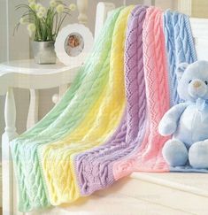 a blue teddy bear sitting on a white bench next to a multicolored blanket