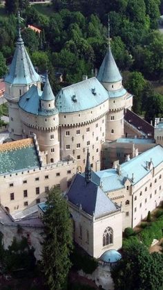 an aerial view of a castle with blue roof tops and green trees in the background