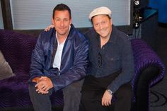 two men sitting on a purple couch in front of a tv screen and smiling at the camera