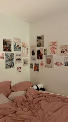 an unmade bed with pink sheets and posters on the wall