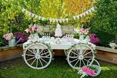 a table with flowers and cake on it in the middle of a garden surrounded by greenery