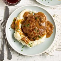 two white plates topped with mashed potatoes covered in gravy and meatballs