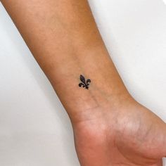 a small black fleur de lis tattoo on the wrist