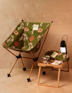 a small table with a lamp on top of it next to a green chair covered in a flowered fabric