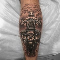 a man's leg with a black and grey tattoo design on it, featuring an image of a motorcyclist