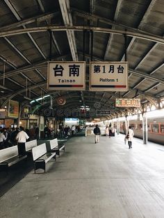 people are walking through the train station with benches and signs hanging from the ceiling above them