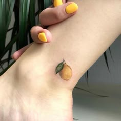 a woman's foot with yellow nail polish and a small orange tattoo on it