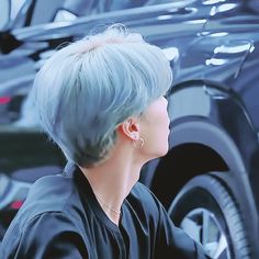 a woman with blue hair is sitting in front of a black car and looking off into the distance