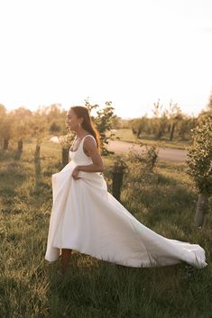 a woman in a white dress is walking through the grass