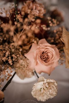 an arrangement of flowers in a white vase on a table with other items around it