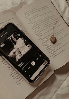 an open book with a cell phone sitting on top of it next to a necklace