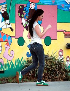 a woman walking down the sidewalk in front of a colorful wall