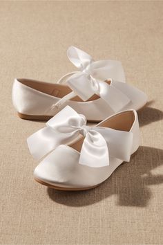 two pairs of white shoes with bows on the front and back, sitting on a beige surface