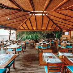 the inside of a restaurant with tables and chairs covered in bamboo roofing overlooking the ocean