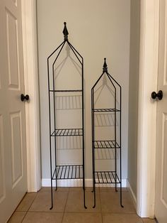 two black metal shelves sitting next to each other on top of a tile floor in front of a door