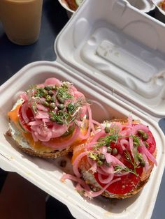 two open faced sandwiches with tomatoes, onions and capers in a styrofoam container