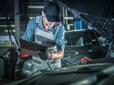 a man working on an engine in a car garage with his laptop and wrench