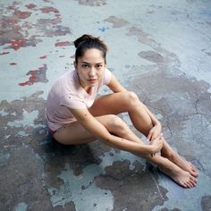 a woman is sitting on the ground with her legs crossed and looking at the camera