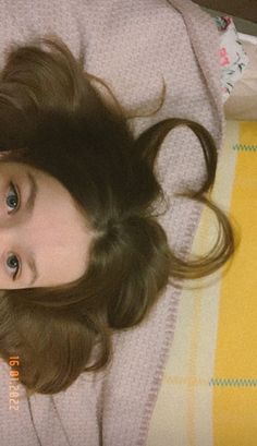 a young woman laying on top of a bed next to a yellow blanket and remote control