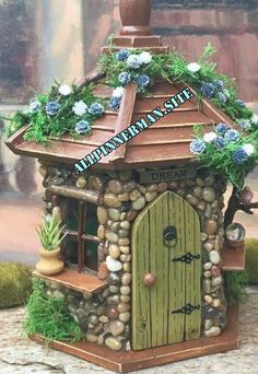 a small house made out of rocks and stones with blue flowers on the roof is shown