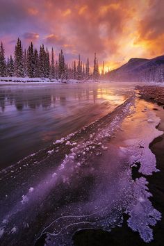 the sun is setting over a lake with ice and snow on the ground in front of it