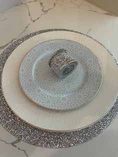 a white plate topped with a ring on top of it next to a silver and white plate