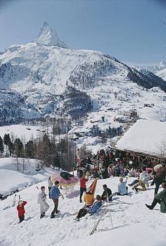 a group of people standing on top of a snow covered slope next to a mountain