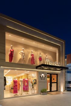 a store front with mannequins and dresses on display in the windows at night