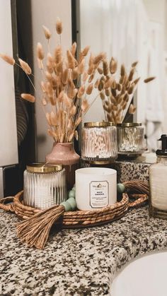 a bathroom counter topped with candles and vases filled with dried flowers next to a mirror