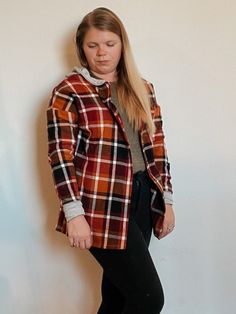 a woman standing in front of a wall wearing black pants and a plaid shirt with long sleeves