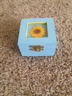 a small blue box with a yellow flower in it on the floor next to carpet