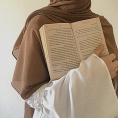 a woman wearing a hijab and holding an open book