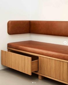 a brown bench with drawers underneath it in a white walled room next to a wall