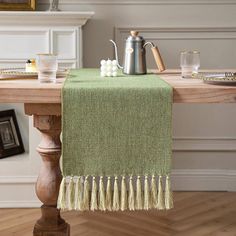 a green table runner with tassels sits on top of a wooden dining table