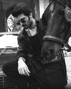 a man sitting next to a horse in front of a car and wearing sunglasses on his head