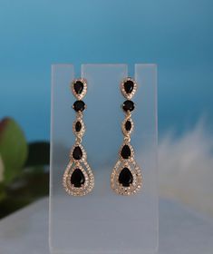 These earrings boast a bold pear-shaped design, embellished with deep black cubic zirconia (CZ) stones that offer a striking contrast. The dangling construction allows them to swing gracefully with every movement, adding a sophisticated and edgy flair to any ensemble. Length: 2 inches Width: 0.50 inches Closure: Bullet with Disc Backs Material: Brass with 18K Gold Plating with Rhodium Coating Lead Free and Hypoallergenic Evening Teardrop Chandelier Earrings With Sparkling Stones, Cubic Zirconia Teardrop Earrings For Evening, Evening Teardrop Earrings In Cubic Zirconia, Evening Teardrop Dangle Earrings In Cubic Zirconia, Evening Teardrop Dangle Earrings With Cubic Zirconia, Pear-shaped Cubic Zirconia Chandelier Earrings For Party, Sparkling Teardrop Earrings For Evening, Evening Pear-shaped Cubic Zirconia Earrings, Teardrop Pendant Earrings With Sparkling Stones For Party