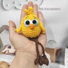 a hand holding a small crocheted yellow bird with blue eyes and a brown string