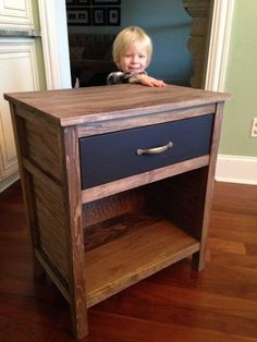 a young boy standing in front of a wooden table with drawers on top of it