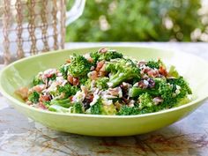 a green bowl filled with lots of broccoli and other food on top of a table