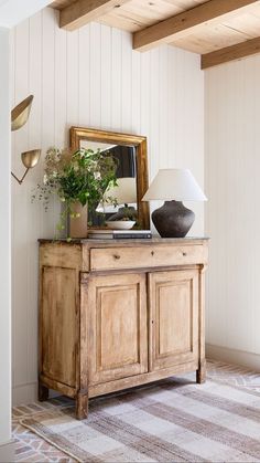 a wooden dresser sitting in front of a mirror on top of a wall next to a lamp