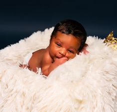 a baby is smiling while laying on a fluffy white blanket with a golden crown on it's head