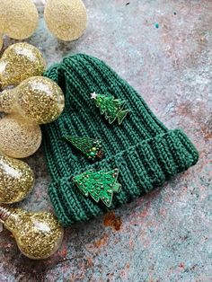 a green knitted beanie with christmas trees on it and gold ornaments around it