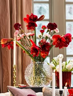 a vase filled with red flowers sitting on top of a table next to two candles