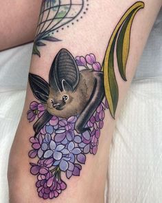 a bat on the leg with flowers and leaves around its neck is seen in this tattoo design