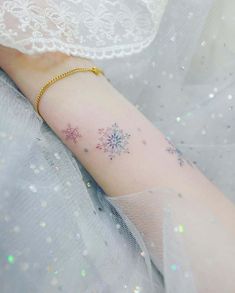 a snowflake tattoo on the left forearm and right arm, with glitters all around it