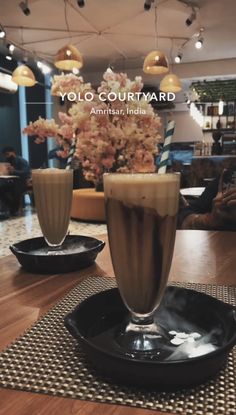 two drinks sitting on top of a black plate next to each other in front of a flower vase