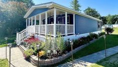 a blue mobile home with white railings on the front porch and landscaping around it