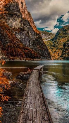 a wooden dock sitting on top of a lake surrounded by mountains in the fall time